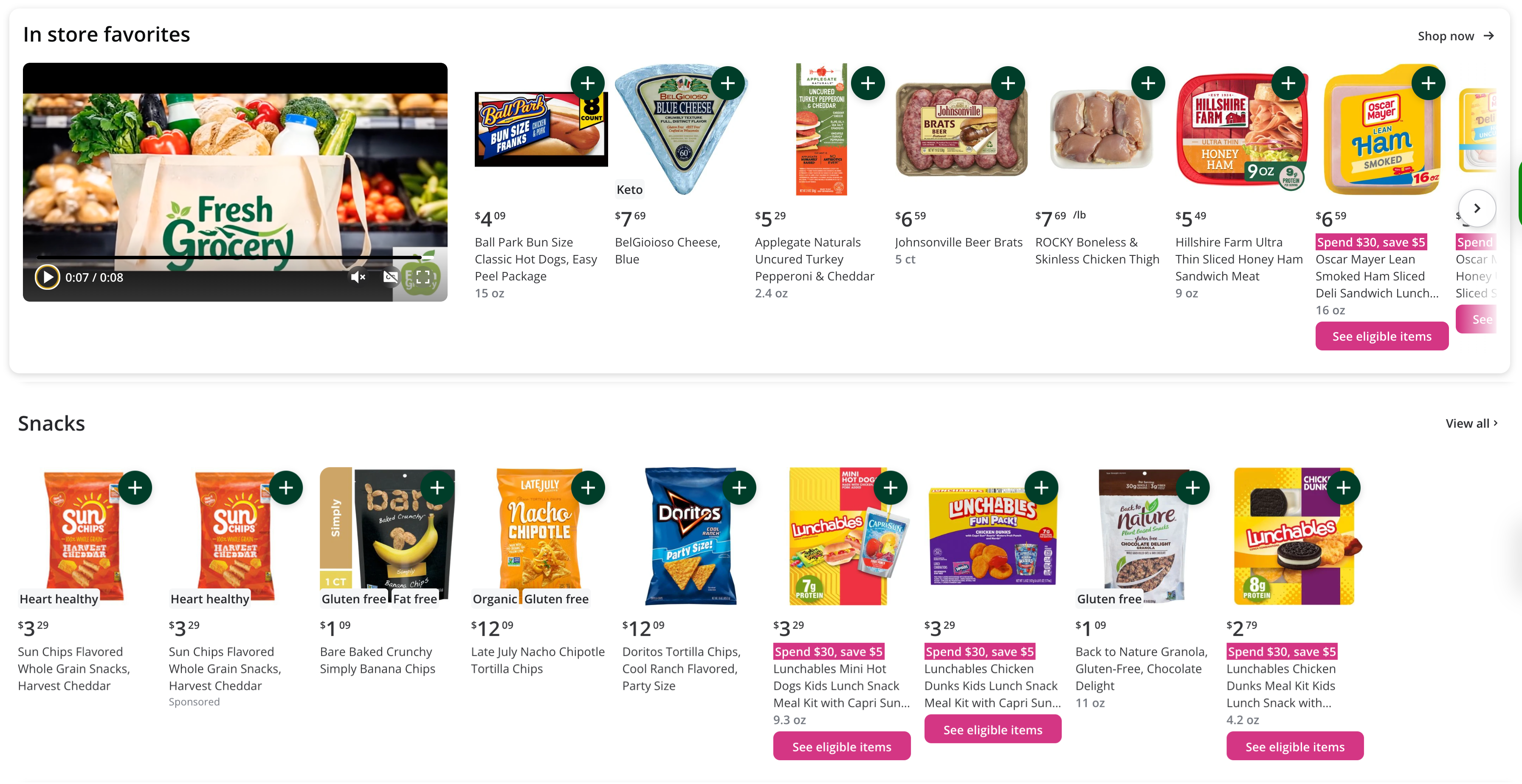 Shows a grocery store page highlighting products in two sections: &quot;In store favorites&quot; and &quot;Snacks.&quot; The top section includes a looping video showcasing fresh groceries and displays items such as hot dogs, blue cheese, chicken thighs, and deli meat, with prices and an option to shop. The &quot;Snacks&quot; section lists various snack items like Sun Chips, banana chips, and Lunchables, with tags indicating categories like heart-healthy or gluten-free, along with promotional offers.